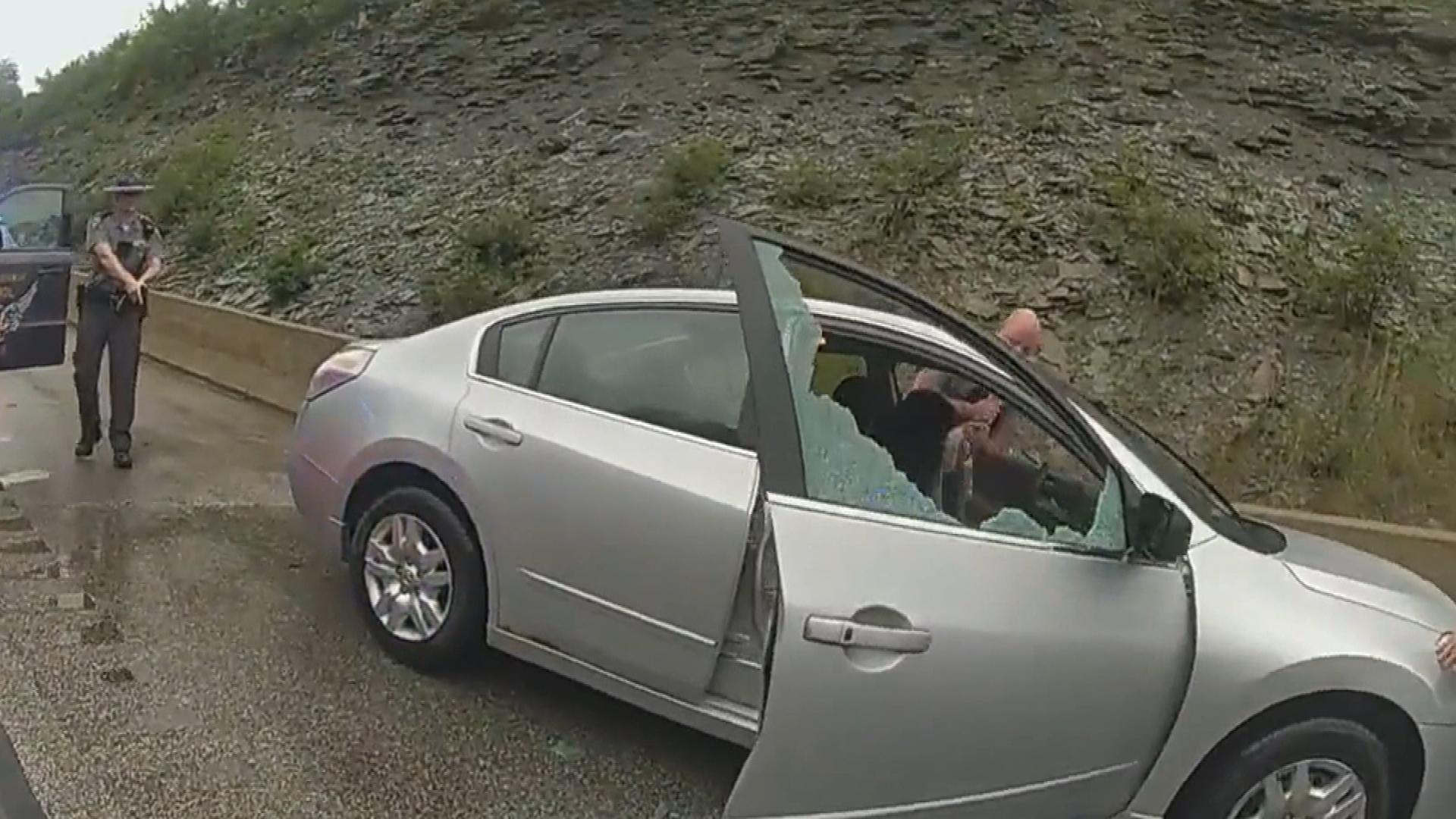 State troopers surround car with smashed window.