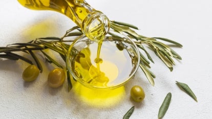 Jar of olive oil and olive branches on white background