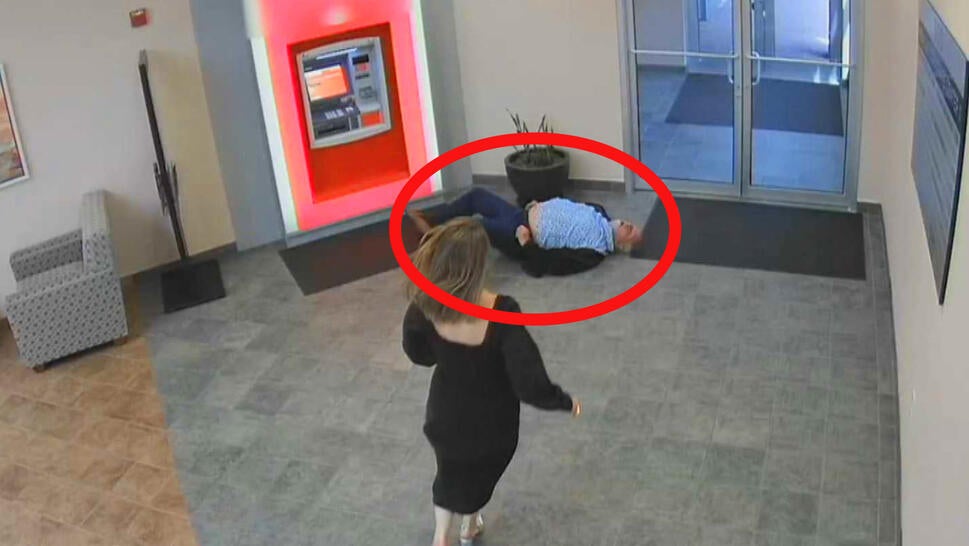 Building lobby with a man lying on the floor in front of an ATM, circled in red. A woman is running toward him in a black dress.
